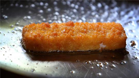 Ein Fischstäbchen wird in einer Pfanne gebraten.
