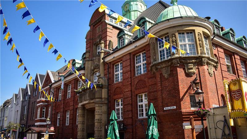 Das Foto aus dem Jahr 2025 zeigt Girlanden in den Buxtehuder Stadtfarben Blau und Gelb. Regelmäßig im Frühling und Sommer verschönern die Wimpel den Platz vor dem Rathaus (Foto) sowie Wege in der Innenstadt.