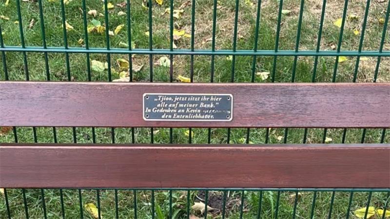 Das Foto zeigt die erste Gedenkplakette an der Holzbank am Mühlenteich, bevor Unbekannte sie gewaltsam entfernt haben.