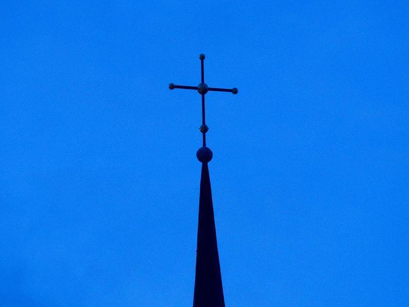 Das Kreuz einer Kirche ist in der Abenddämmerung zu sehen. Foto: Friso Gentsch/dpa/Symbolbild