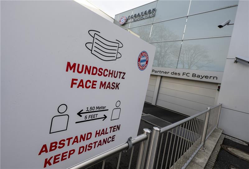 Das Logo des FC Bayern München und der Hinweis auf Mundschutz und Abstandsregel sind auf einem Schild am Hauptgebäude des Fußball-Vereins zu sehen. Vor Beginn des Trainingsauftakts beim Rekordmeister wurden mehrere Spieler positiv auf Corona getestet. Foto: Peter Kneffel/dpa