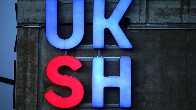 Das Logo des Universitätskrankenhauses Schleswig-Holstein (UKSH) ist an einer Fassade des Krankenhauses beleuchtet.