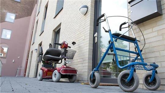 Ein Krankenfahrstuhl und ein Rollator stehen vor einem Wohnhaus.