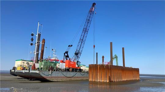 Das Transportschiff brachte Bagger und Arbeitsgeräte zum Einsatzort im Watt. Die Grube schützen Spundwände gegen die Flut.
