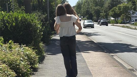 Das ist dreifach verboten. Die beiden Mädchen fahren zu zweit auf einem Roller, sind auf der falschen Straßenseite als Geisterfahrerinnen unterwegs und benutzen den Fußweg statt des Radwegs.