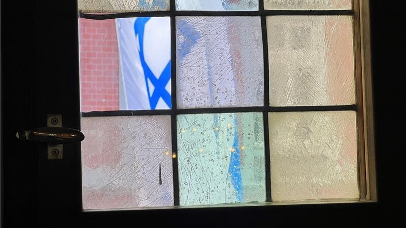 Das kaputte kleine Fenster im Stader Rathaus - dahinter weht über der Fußgängerzone die Flagge Israels. 