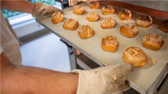 Ein Mitarbeiter schiebt in der Bäcker-Innung Berlin Blech mit Brötchen in den Ofen. 