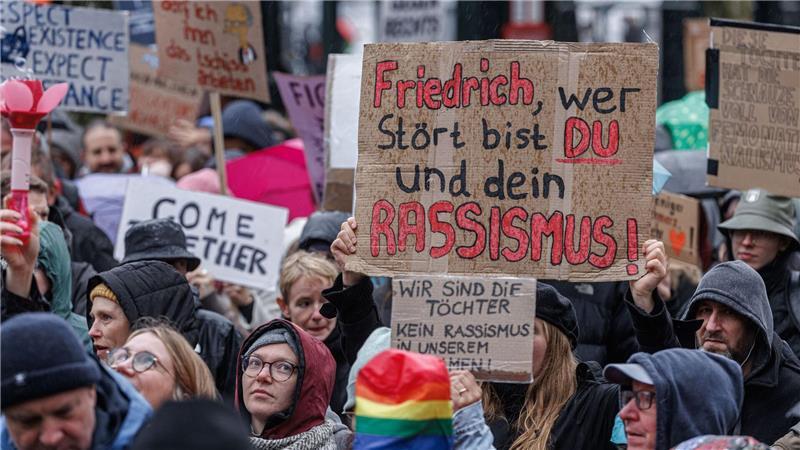 Rund 2.000 Menschen protestieren gegen „Stadtbild“-Äußerung Demonstranten halten im Regen Schilder mit Parolen gegen Bundeskanzler Friedrich Merz hoch.