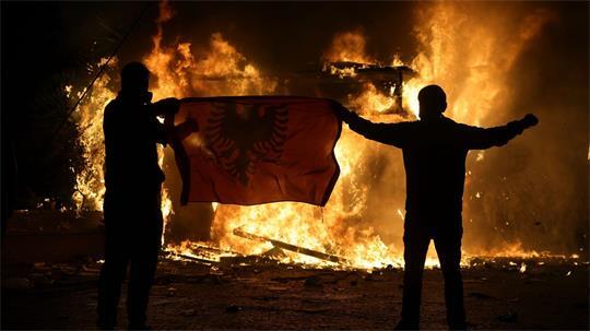 Demonstranten halten während Ausschreitungen in Tirana eine albanische Fahne vor einem brennenden Tabakladen hoch, als sich Studenten einer regierungsfeindlichen Demonstration anschließen.