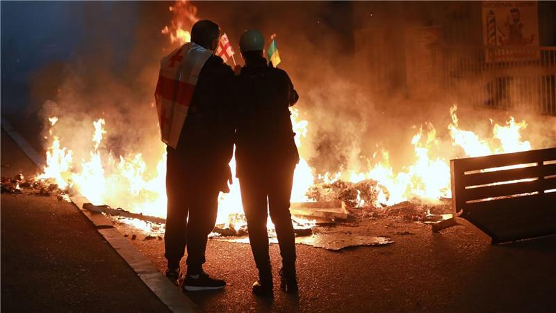 Demonstranten mit einer georgischen und einer ukrainischen Nationalflagge stehen im Stadtzentrum von Tiflis hinter einer brennenden Barrikade während einer Kundgebung der Opposition, bei der sie die Kommunalwahlen boykottieren und die Freilassung politischer Gegner fordern. 