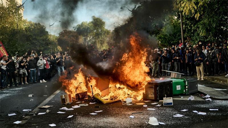 Demonstranten stehen bei Protesten um brennende Mülltonnen.
