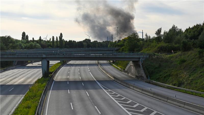 Große Rauchsäule über Veddel: Feuer im Hamburger Hafen – Drei Verletzte Der Abschnitt der Autobahn A1 in Hamburg-Moorfleet ist nach der Räumung durch Polizei und Feuerwehr frei von Autos. Im Hintergrund steigt eine große Rauchwolke in die Luft.
