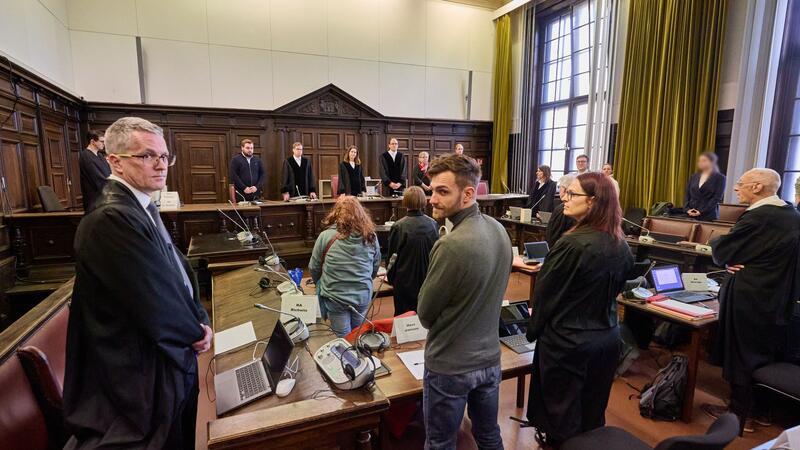 Prozess um Krawalle bei G20: Protest oder Landfriedensbruch? Der Angeklagte Nils Jansen (M), die Richter, Anwälte sowie weitere Angeklagte stehen im Gerichtssaal.