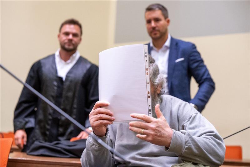 Neuer Prozess um getötete Frau: Gatte bestreitet Mordvorwurf Der Angeklagte hält sich im Gerichtssaal ein Blatt Papier vor das Gesicht. Im Hintergrund stehen seine Anwälte.