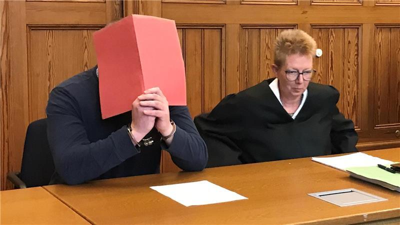 Der Angeklagte im Messerstich-Prozess verdeckt sein Gesicht. Neben ihm sitzt seine Verteidigerin Katrin Bartels.