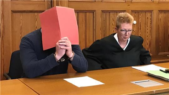 Der Angeklagte im Messerstich-Prozess verdeckt sein Gesicht. Neben ihm sitzt seine Verteidigerin Katrin Bartels.