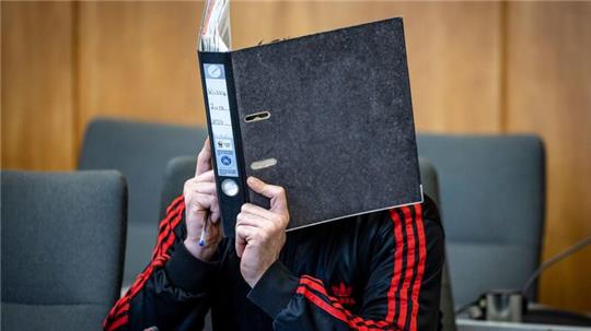 Der Angeklagte verbirgt im Landgericht sein Gesicht hinter einem Aktenordner.