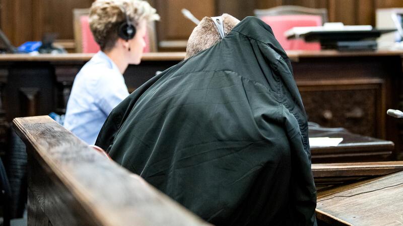 Der Angeklagte verdeckt sein Gesicht mit einer Jacke.