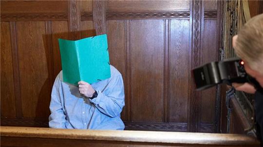 Der Angklagte sitzt im Landgericht Berlin und verbirgt sein Gesicht hinter einem Schnellhefter.