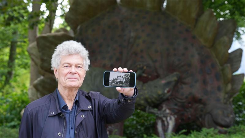 Der Archivar Herman Reichenbach zeigt auf seinem Handy historische Schwarz-Weiß-Fotos der Dino-Skulpturen.