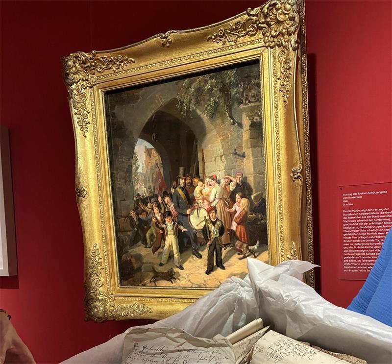 Drei Frauen entdecken Schatz der Buxtehuder Schützengilde von 1539 Der „Auszug der kleinen Schützengilde von Buxtehude“ ist ein berühmtes Gemälde des Hamburger Künstlers Johann Jacob Gensler aus dem Jahr 1840; vorne: Schriftstücke aus der Schützenlade.