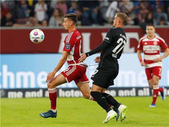 Der Düsseldorfer Yannik Engelhardt (l) und der Osnabrücker Michael Bruno Cuisance kämpfen um den Ball, während die Fans in der ersten Hälfte schweigen.