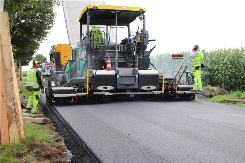 Fertiger macht die Kreisstraße fast fertig Der Fertiger verteilt den etwa 170 Grad heißen Asphalt auf der Tragschicht. Fotos: Klempow