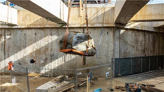 Der Findling wird aus der Baugrube gehoben.