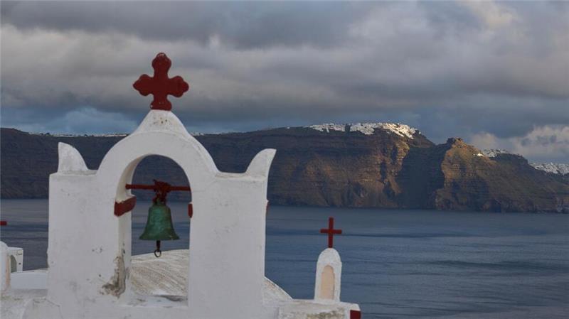 Der Glockenturm einer orthodoxen Kirche in Oia auf der erdbebengeschädigten Insel Santorini, im Hintergrund der Hauptort Fira. 