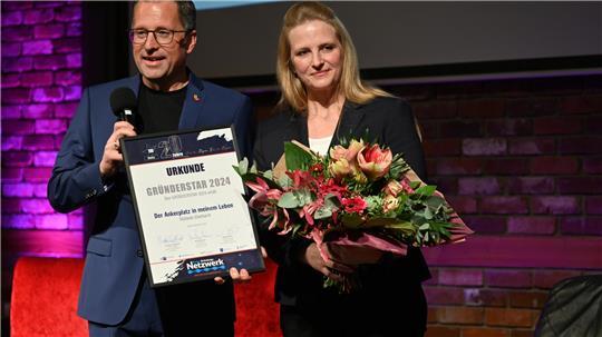 Der Gründerstar 2024: Stefanie Eberhardt mit ihrem Ankerplatz am Fähranleger Wischhafen. Landrat Kai Seefried gratuliert.