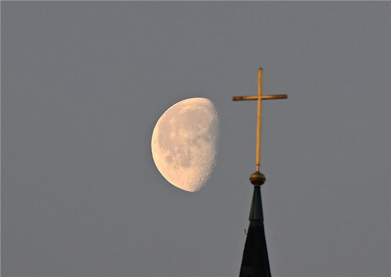 Studie zu Missbrauch in evangelischer Kirche im Januar Der Mond steht im Morgenlicht hinter einem Kreuz auf einem Kirchturm.