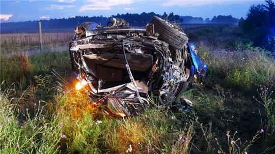 Ein schwerbeschädigtes Auto liegt auf dem Dach in einem Feld. 