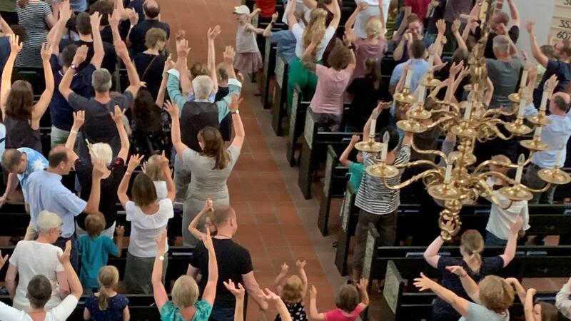 Die Besucher des Familienkonzerts sitzen nicht still in den Bänken, sondern stehen zwischen den Bänken, halten die Hände in die Höhe und bewegen diese zur Musik