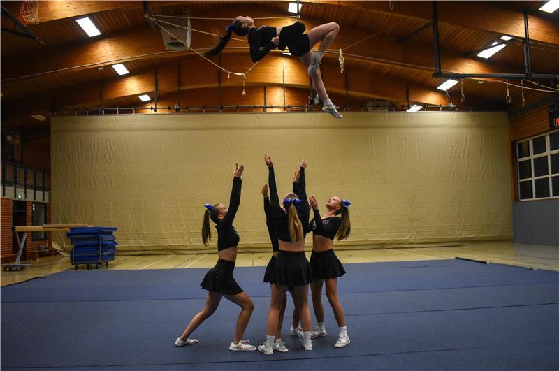 Hollywood-Glitzer: Wiepenkathen tritt in den USA und gegen Klischees an Eine Cheerleaderin macht einen „Pike Pretty Basket“ und fliegt in der Luft, vier andere auf einer Bodenmatte stehen bereit, um sie aufzufangen.