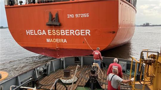 Der Schlepper Bützfleth hat sich auf der Elbe kurz vor dem Seehafen Stade an die Helga Essberger gehängt. Im Hauptfahrwaser kommt ihnen ein großes Containerschiff entgegegen Richtung Nordsee.