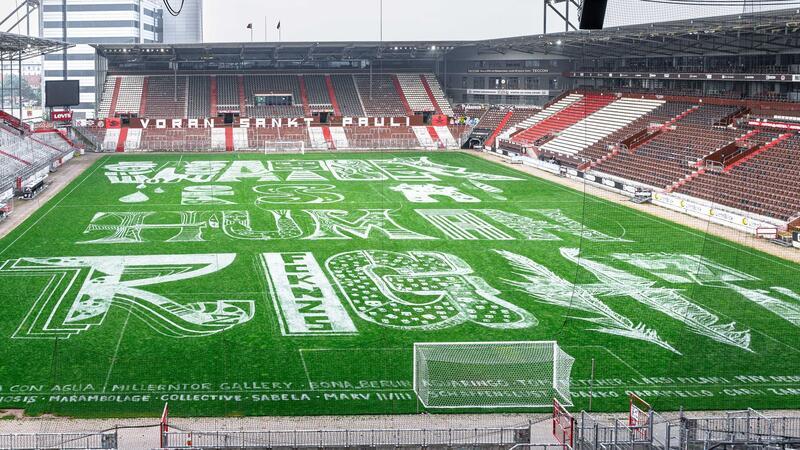 Millerntor Gallery verwandelt Stadion in Festivallandschaft Der Schriftzug „Water Is A Human Right“ wurde aus Rasenmarkierungsfarbe über Nacht auf dem Spielfeld im Millerntor-Stadion aufgebracht. Teilnehmende Künstler und Künstlerinnen des Millerntor Galerie Festivals, das am 31. Mai beginnt, haben jeweils die Buchstaben individuell gestaltet.