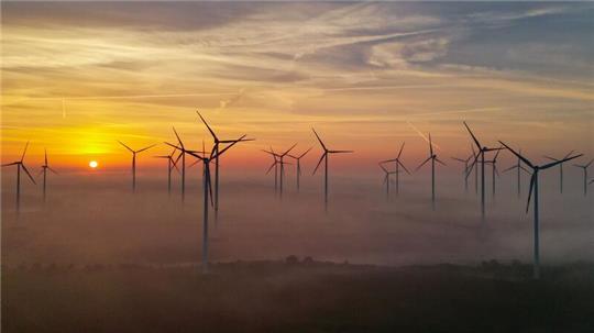 Der Sonnenaufgang scheint durch den Morgennebel über einem Windenergiepark.