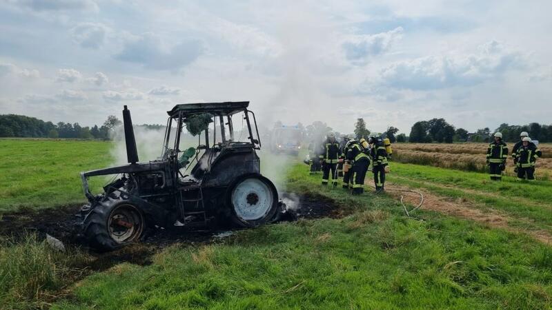 Trecker brennt in Oederquart lichterloh - Landwirt verhindert Desaster Der ausgebrannte Trecker, daneben stehen Feuerwehrleute.