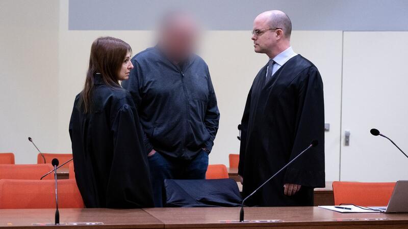Der angeklagte Lokführer (M) steht mit seiner Anwältin und seinem Anwalt im Gerichtssaal in München.