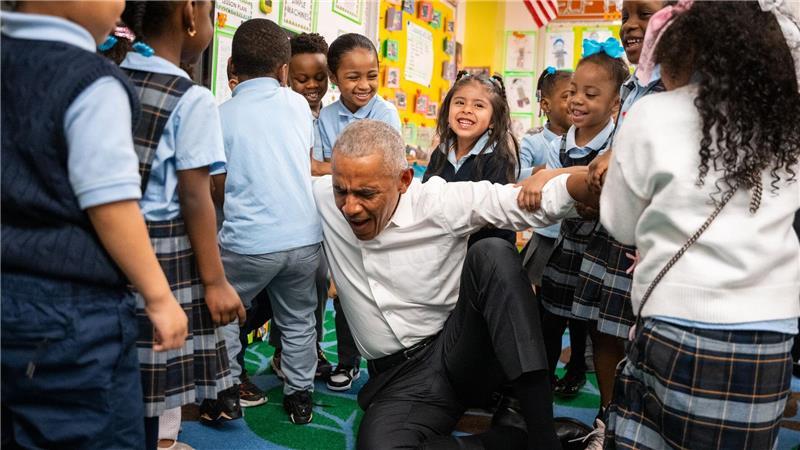 Der frühere US-Präsident Barack Obama lässt sich beim Aufstehen von Kindern hochheben.