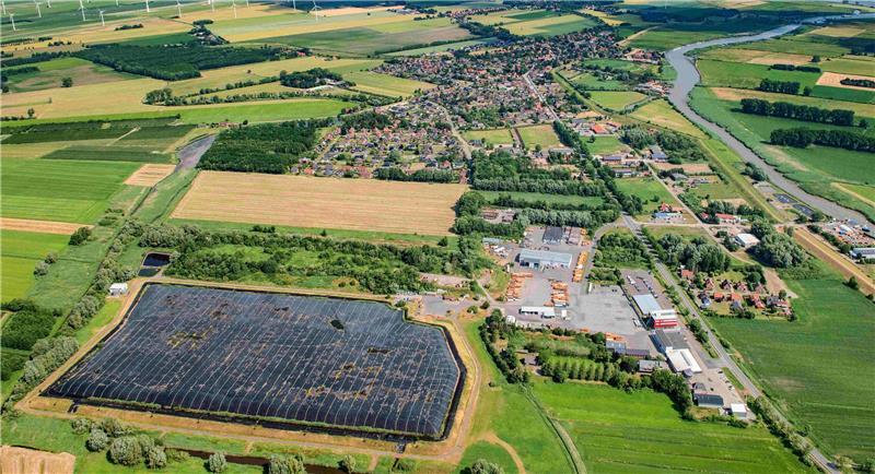 Der mit schwarzer Folie eingedeckte Bereich ist die Deponie Wischhafen II. Oberhalb auf der bewachsenen Fläche befindet sich die stillgelegte Deponie Wischhafen I. Das Karl-Meyer-Firmengelände liegt rechts von der Deponie. Der Ort Wischhafen ist oben zu sehen.