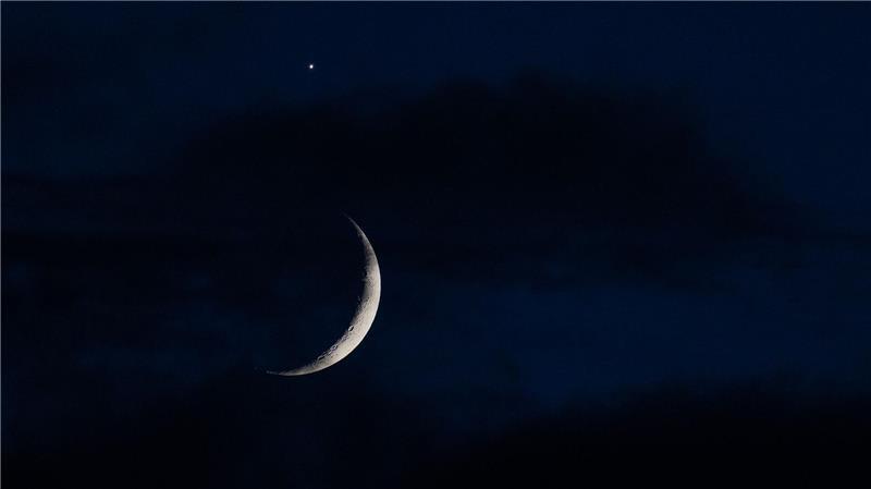 Der sichelförmige Mond wird am Abend hinter Wolken über Köln von der Venus (oben) begleitet.