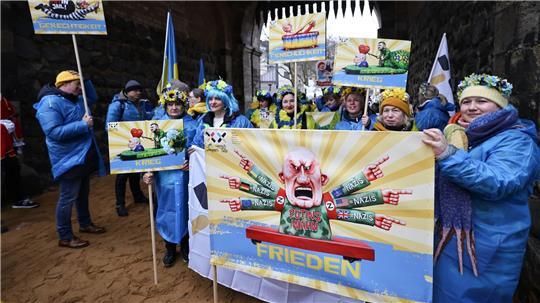 Der ukrainische Hilfsverein Blau-Gelbes-Kreuz hält Plakate mit Putin-Motiven hoch. Das ist als Zeichen der Solidarität mit Wagenbauer Jacques Tilly gemeint. Dieser wird in Russland strafrechtlich verfolgt. 