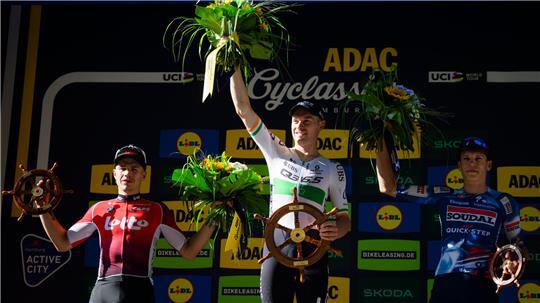 Der zweitplatzierte Belgier Arnaud De Lie vom Team Lotto (l-r) der Sieger aus Irland Rory Townsend vom Q36.5 Pro Cycling Team und der Drittplatzierte Franzose Paul Magnier vom Soudal Quick-Step stehen nach dem Rennen während der Siegerehrung auf dem Podium.
