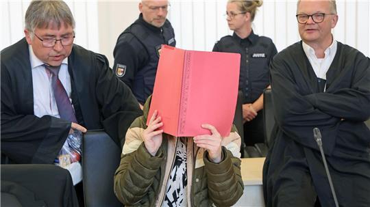 Die Angeklagte sitzt mit Aktendeckel vor dem Gesicht zwischen ihren Verteidigern Andreas Ohm (l-r) und Thomas Löcker. 