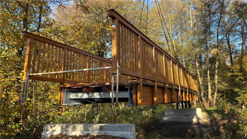 Millimeterarbeit am Kran: Neue Holzbrücke schwebt über die Aue Die Auebrücke kurz vor dem Niederlassen auf die Betonfundamente.