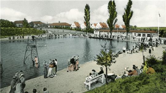 Die Aufnahme zeigt das Freibad in Buxtehude im Jahr 1959. Ein Sandstrand ist am Badeteich aufgeschüttet. Hüte sind bei den Besuchern und Besucherinnen in Mode und schützen vor der Sonne.