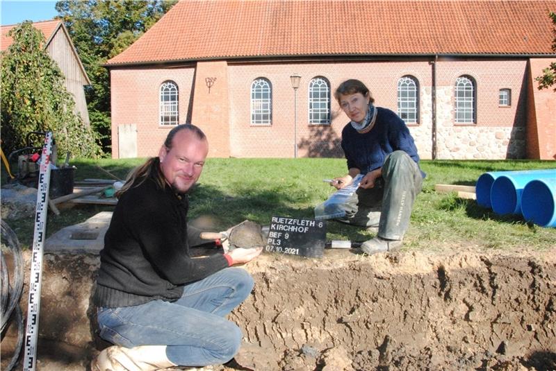 Die Ausgrabungen an der Bützflether Kirche St. Nicolai förderten auch diesen Totenschädel zutage. Alexander Benn und Grabungsleiterin Ulrike Ek dokumentieren den Schädel als weiteres Fundstück. Die leichte Erhöhung hinter ihnen deutet darau
