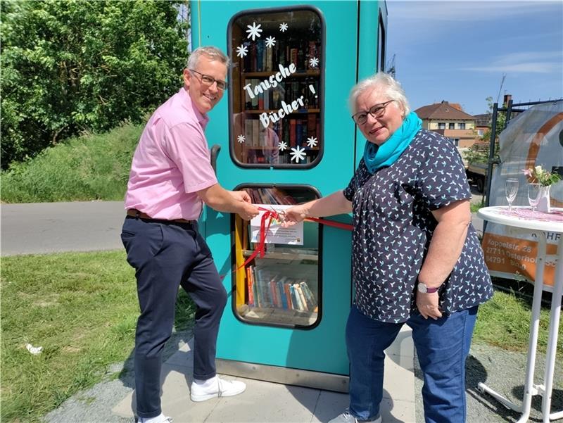 Die Büchertauschbox am Auedamm wird feierlich eingeweiht: Gemeindedirektor Knut Willenbockel und die engagierte Bürgerin Christel Ohse durchtrennen das rote Band. Foto: Lohmann