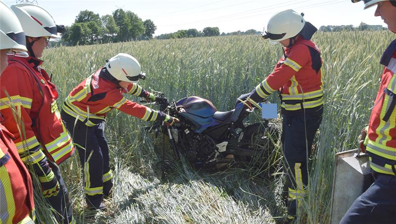 Die Einsatzkräfte ziehen ein Motorrad aus einem Getreidefeld. Foto: Feuerwehr